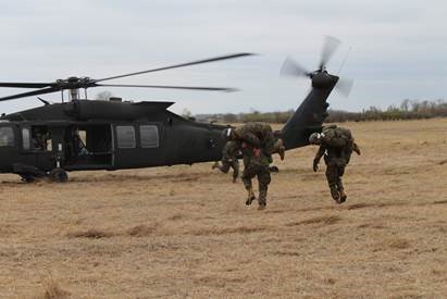 Marines training. Two marines run with other marines across their shoulders to an awaiting helicopter. 